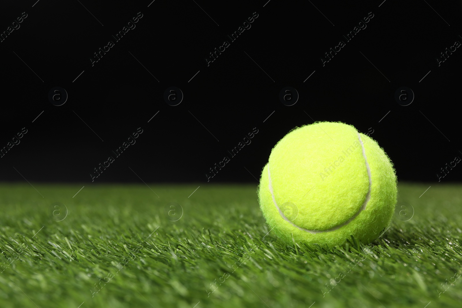 Photo of Tennis ball on green grass against black background, space for text