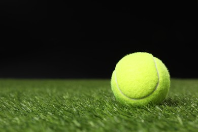 Photo of Tennis ball on green grass against black background, space for text