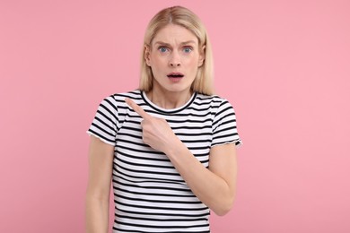 Photo of Surprised woman pointing at something on pink background