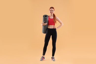 Photo of Young woman in sportswear with fitness mat on beige background