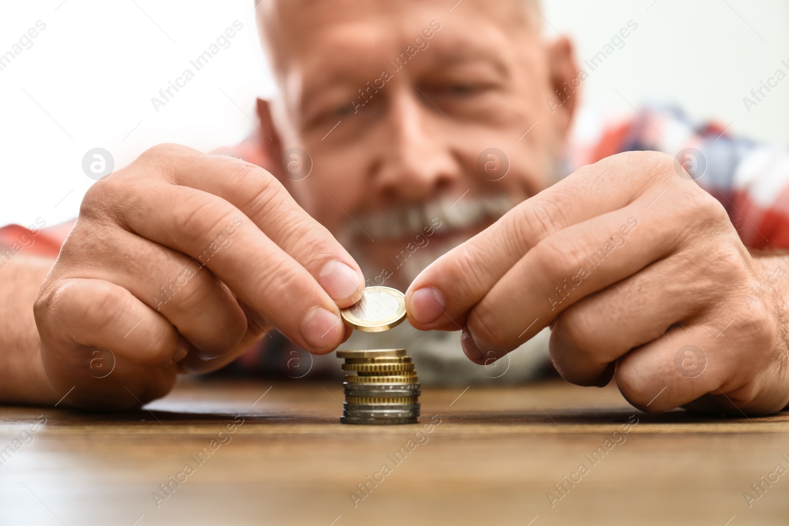 Photo of Senior man stacking up coins at table, focus on hand