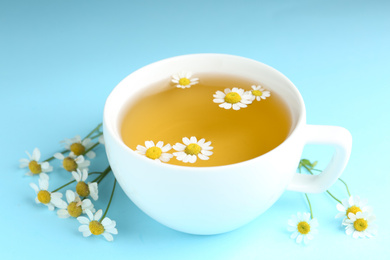 Photo of Cup of tea and chamomile flowers on light blue background