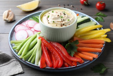 Photo of Fresh raw vegetable sticks and sauce on grey wooden table, closeup