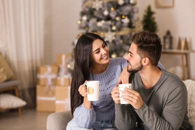 Photo of Happy couple with drinks in living room decorated for Christmas
