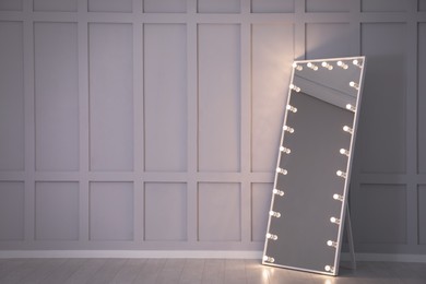 Modern mirror with light bulbs near molding wall in room, space for text