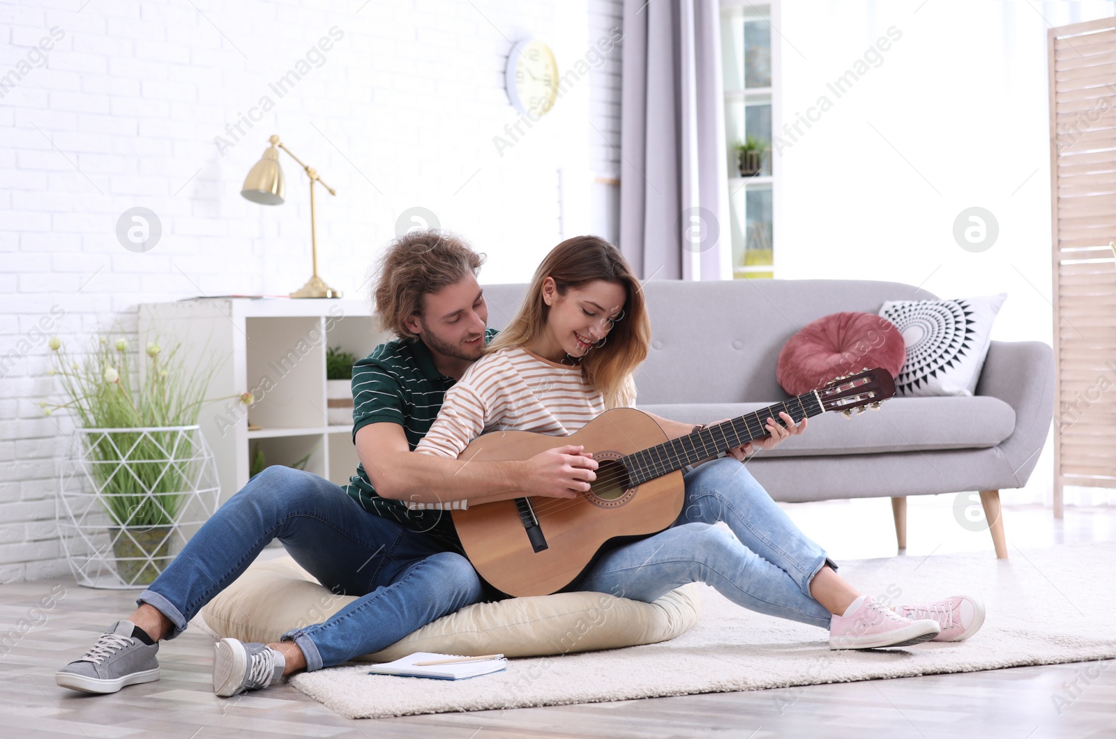 Photo of Young man teaching his girlfriend to play acoustic guitar in living room