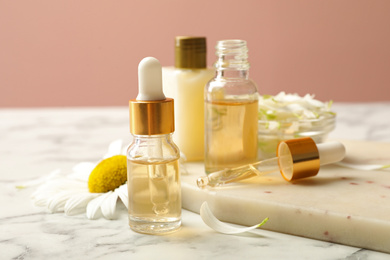 Photo of Chamomile and cosmetic products on white marble table