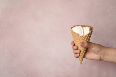 Photo of Woman holding delicious ice cream in wafer cone on pink background, closeup. Space for text