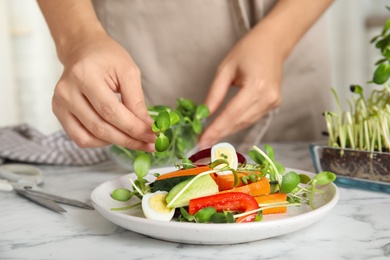 Photo of Woman making salad with fresh organic microgreen at white marble table, closeup