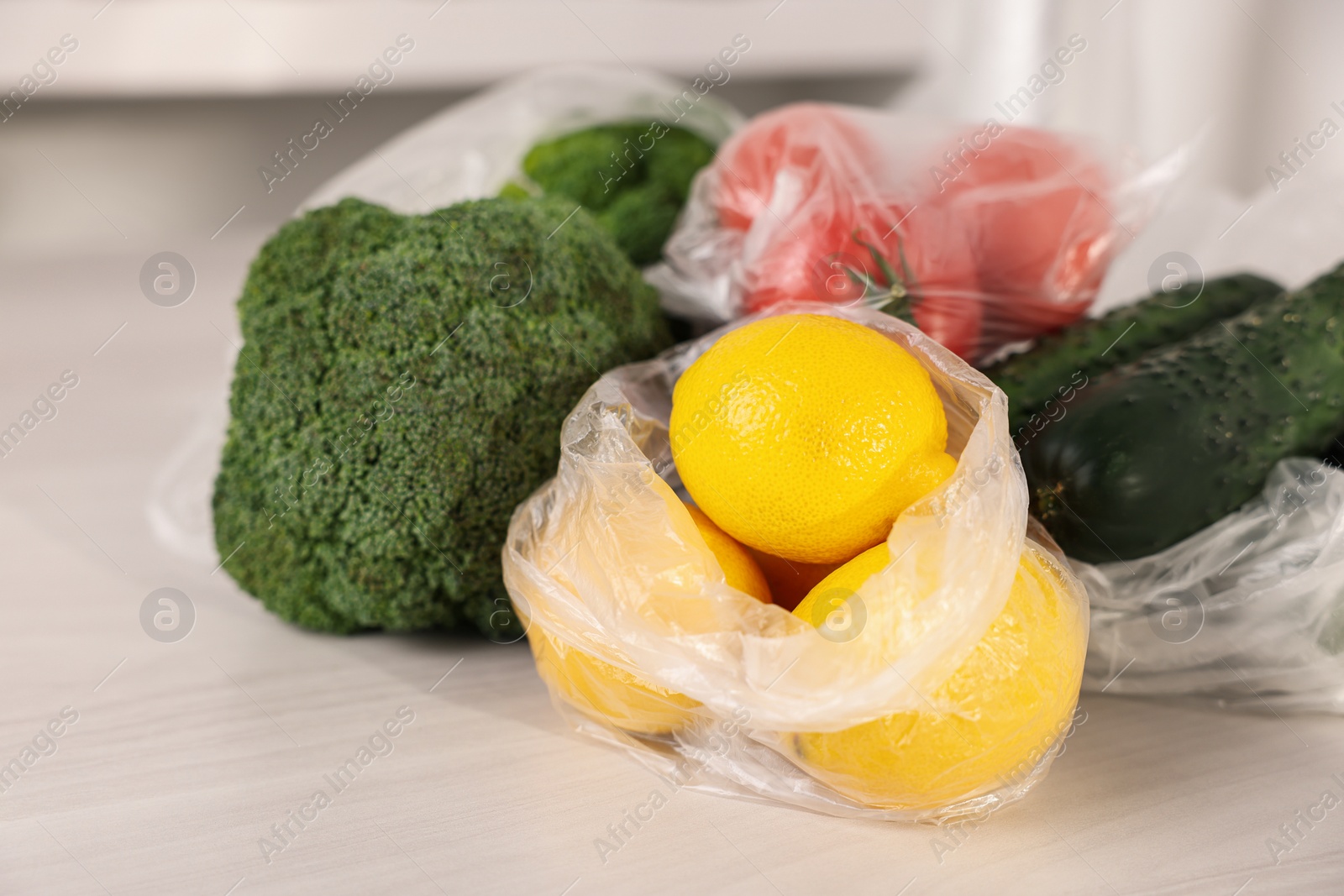 Photo of Plastic bags and fresh products on white table, closeup