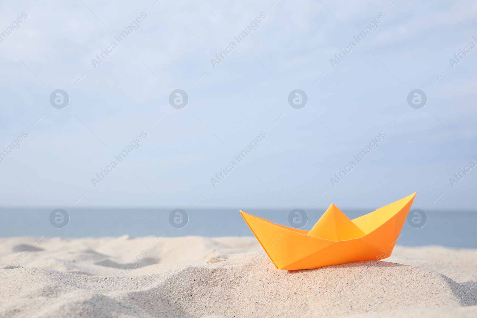 Photo of Orange paper boat on sandy beach near sea, space for text