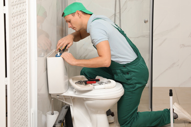 Professional plumber repairing toilet tank in bathroom