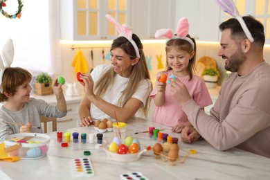 Photo of Easter celebration. Happy family with bunny ears having fun while painting eggs at white marble table in kitchen