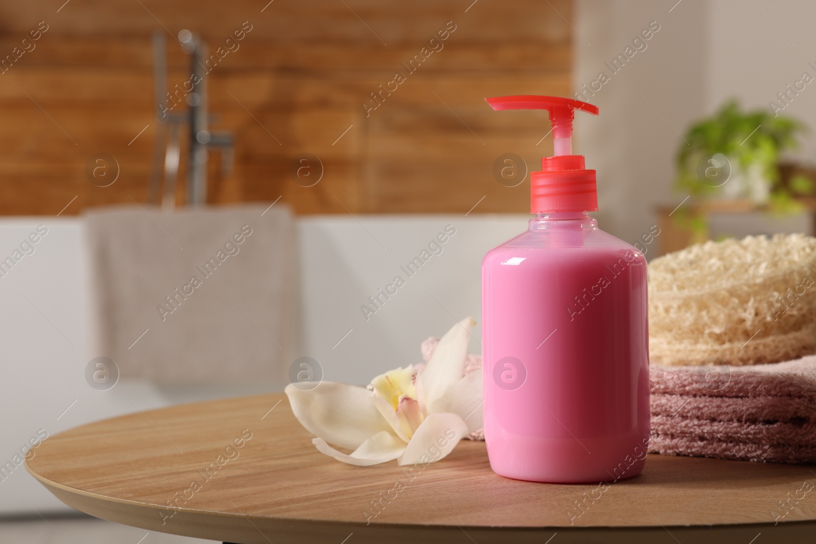 Photo of Dispenser of liquid soap and orchid flower on wooden table in bathroom, space for text