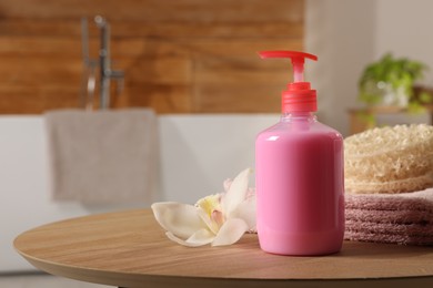 Photo of Dispenser of liquid soap and orchid flower on wooden table in bathroom, space for text