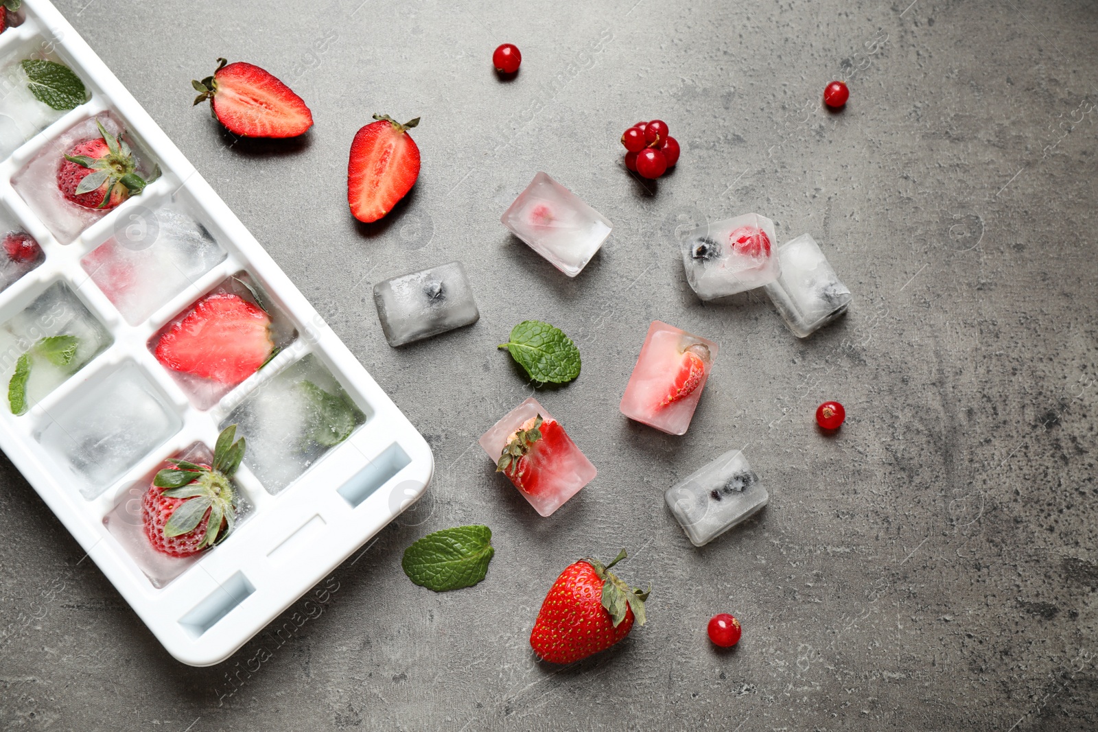 Photo of Ice cubes with berries and tray on grey table, flat lay