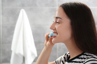 Young woman brushing her teeth with plastic toothbrush in bathroom