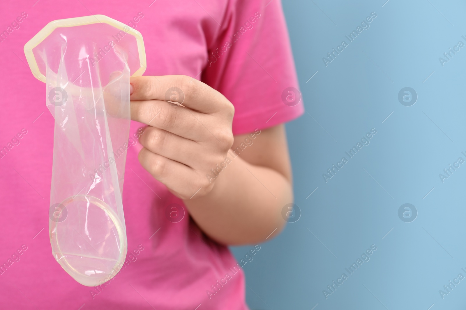 Photo of Woman with unrolled female condom on light blue background, closeup. Space for text
