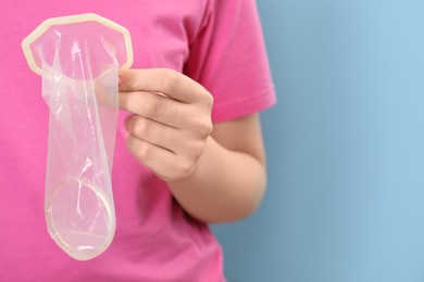 Photo of Woman with unrolled female condom on light blue background, closeup. Space for text