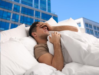 Image of Man in bed and beautiful view of cityscape on background. Poor sleep because of urban noise
