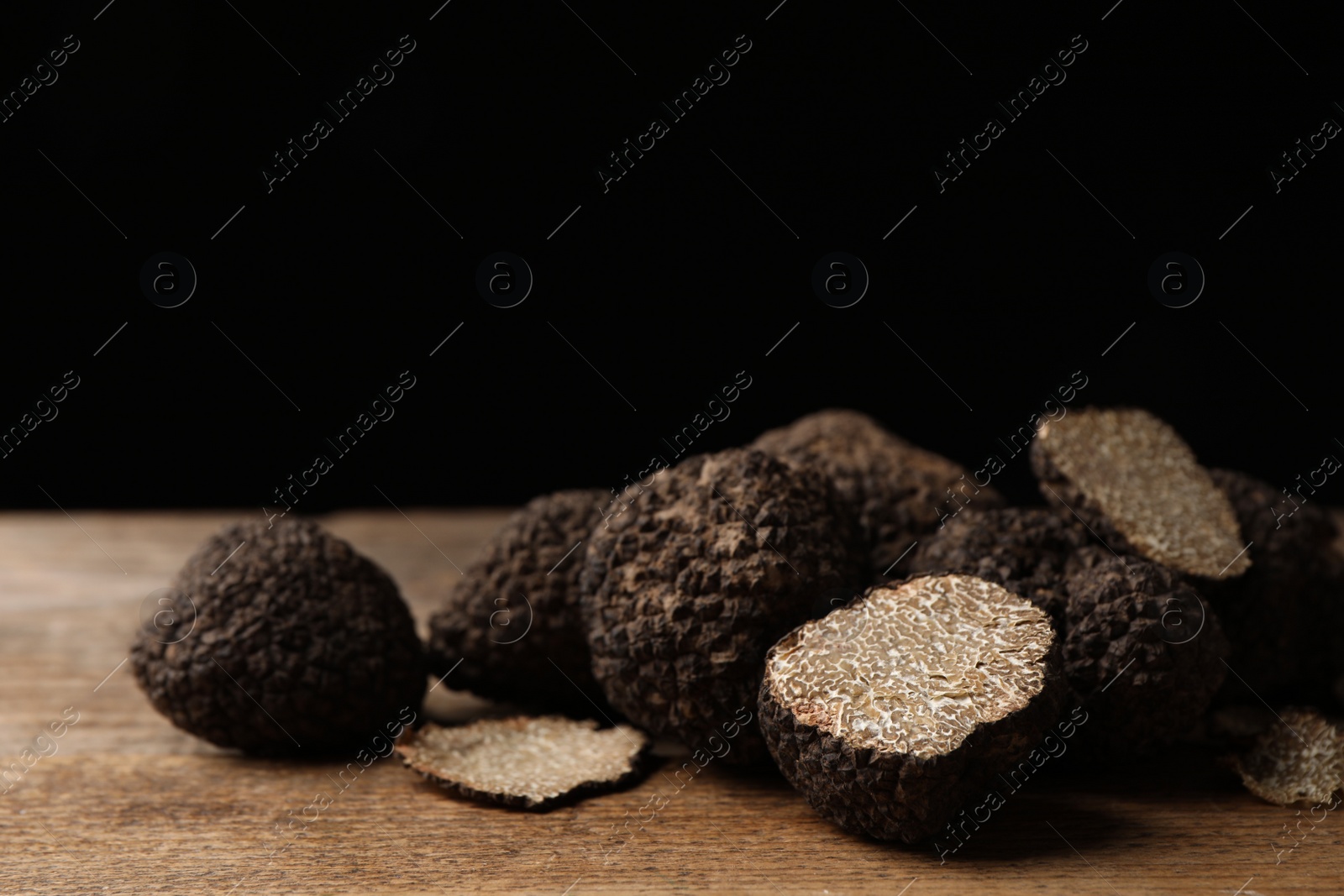 Photo of Whole and cut truffles on wooden table against black background, closeup