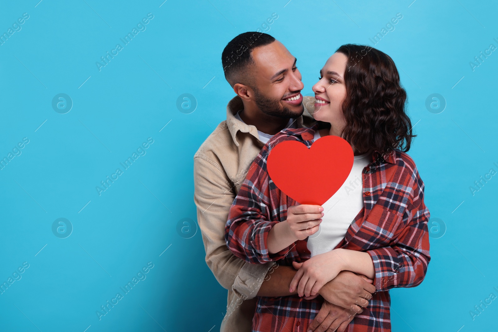 Photo of Lovely couple with red paper heart on light blue background, space for text. Valentine's day celebration