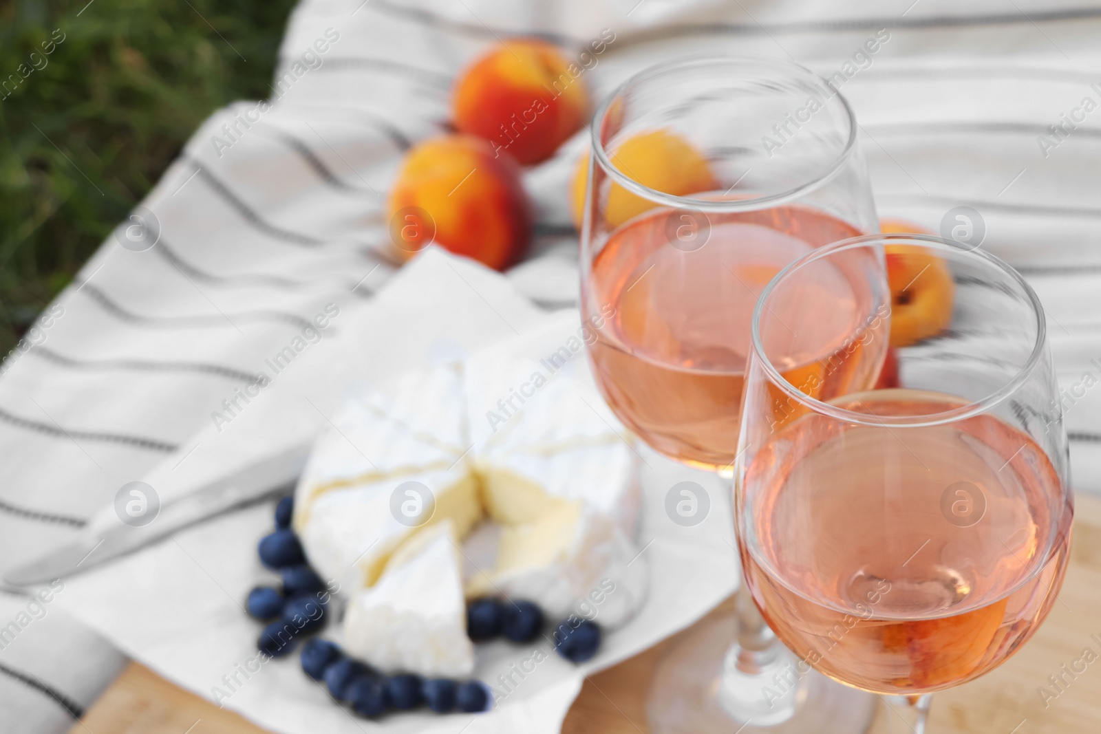 Photo of Glasses of delicious rose wine and food on picnic blanket outdoors, closeup
