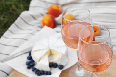 Photo of Glasses of delicious rose wine and food on picnic blanket outdoors, closeup