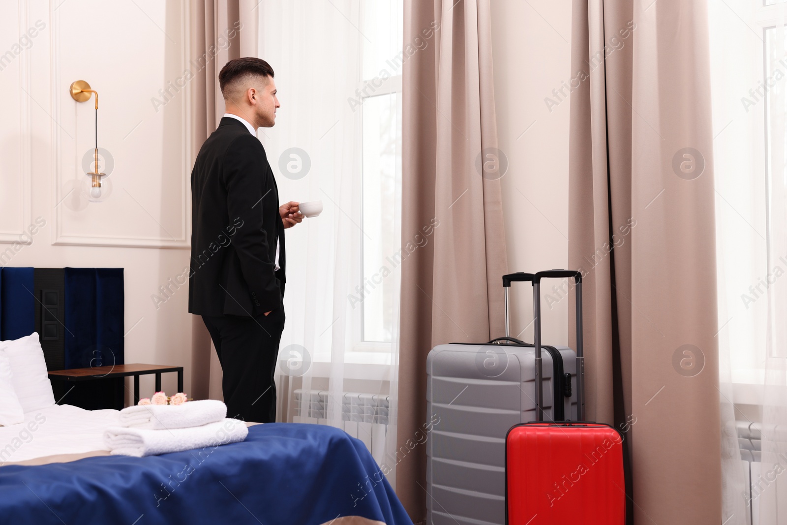 Photo of Handsome businessman drinking coffee near window in hotel room