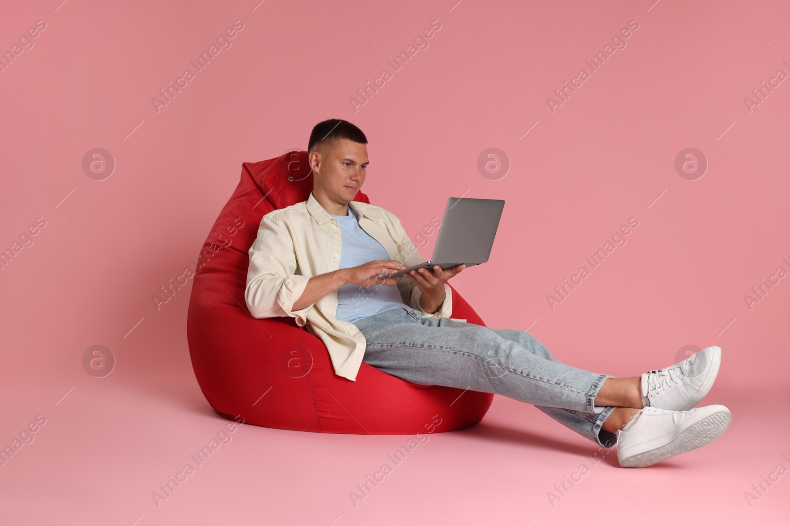 Photo of Handsome man with laptop on red bean bag chair against pink background