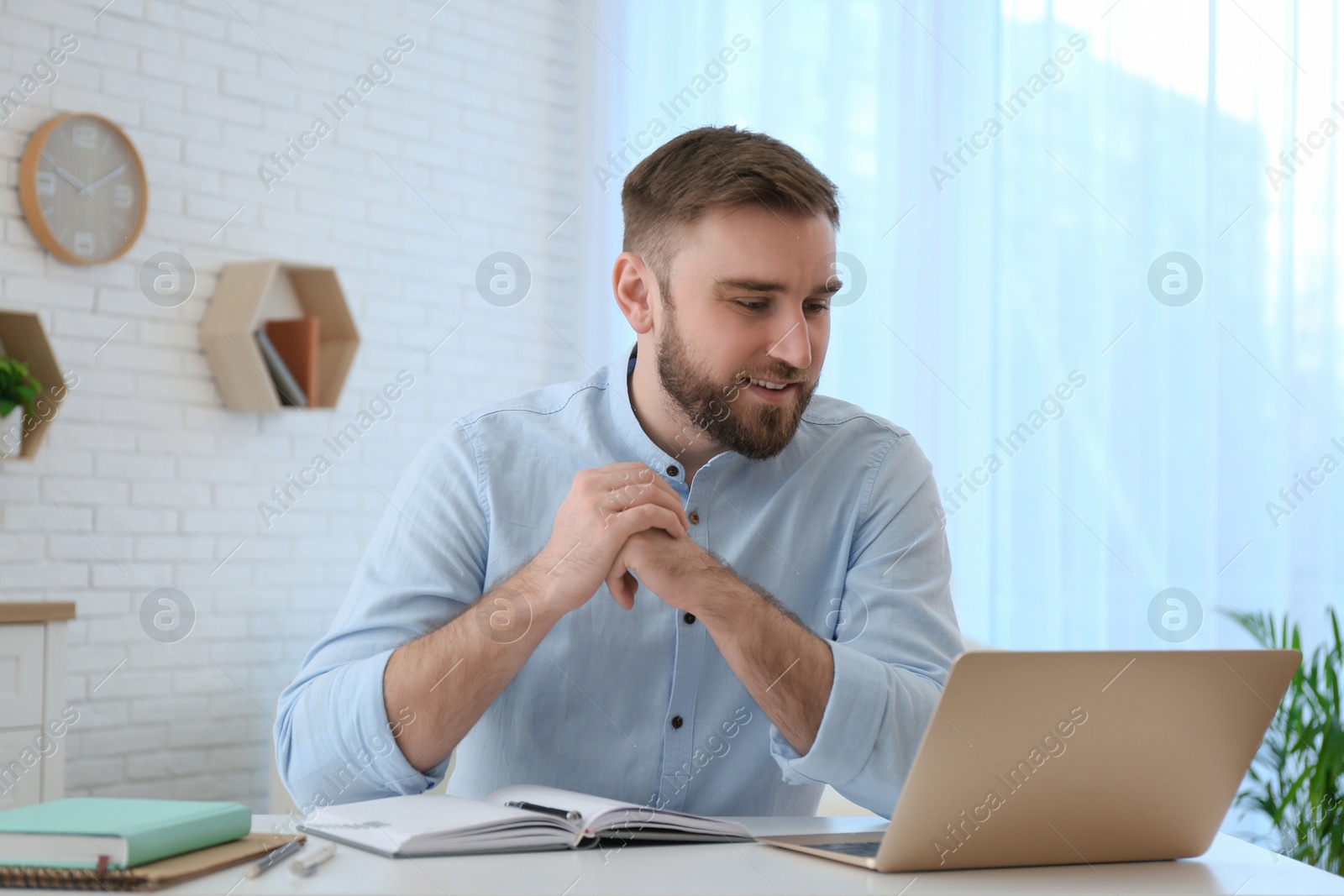 Photo of Young man watching online webinar at table indoors