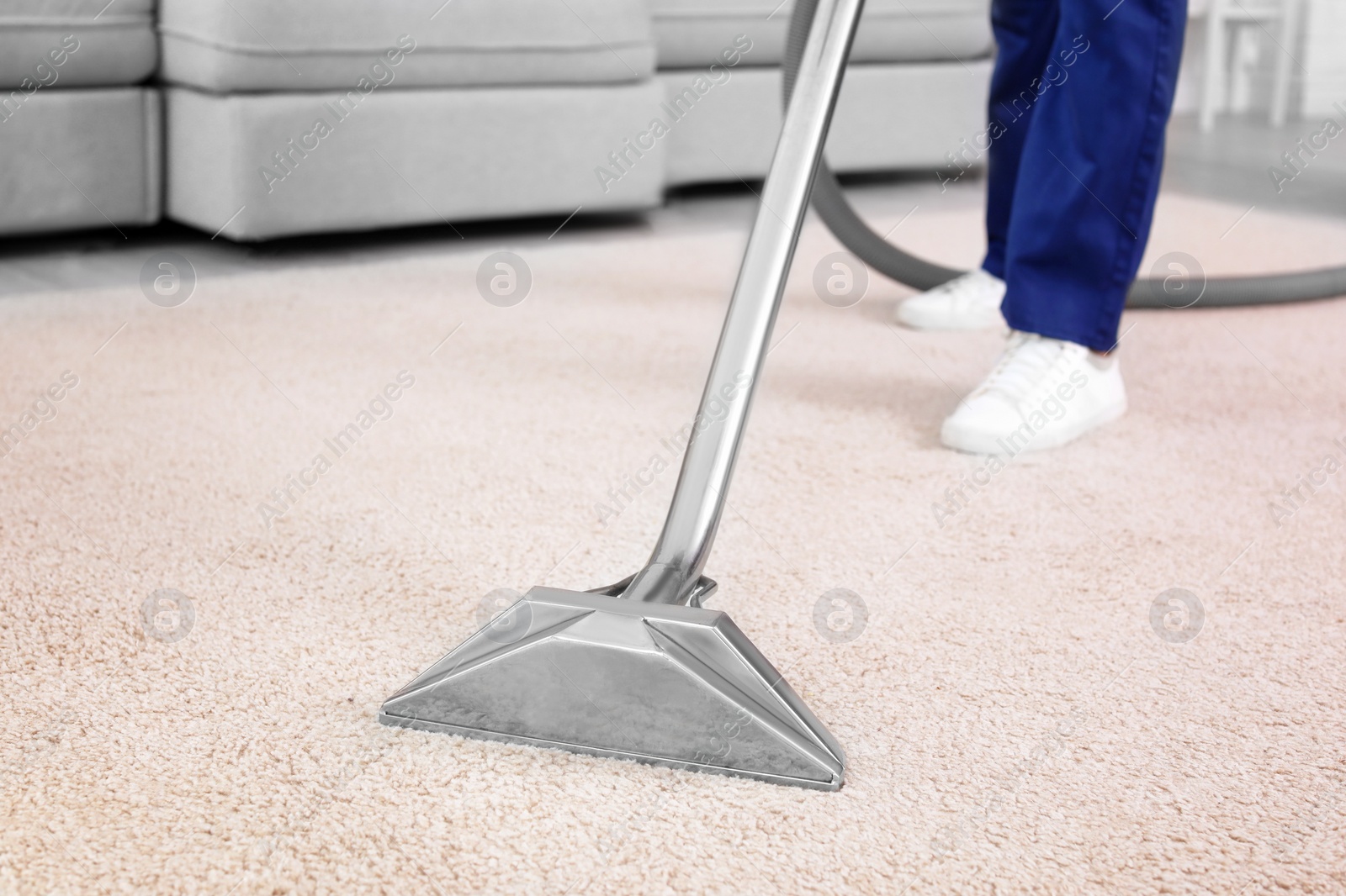 Photo of Male worker removing dirt from carpet with professional vacuum cleaner indoors