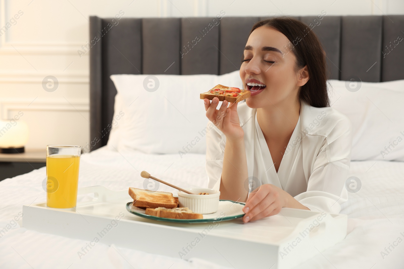 Photo of Happy young woman having breakfast on bed at home