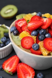 Photo of Delicious fresh fruit salad in bowl and ingredients on dark table, closeup