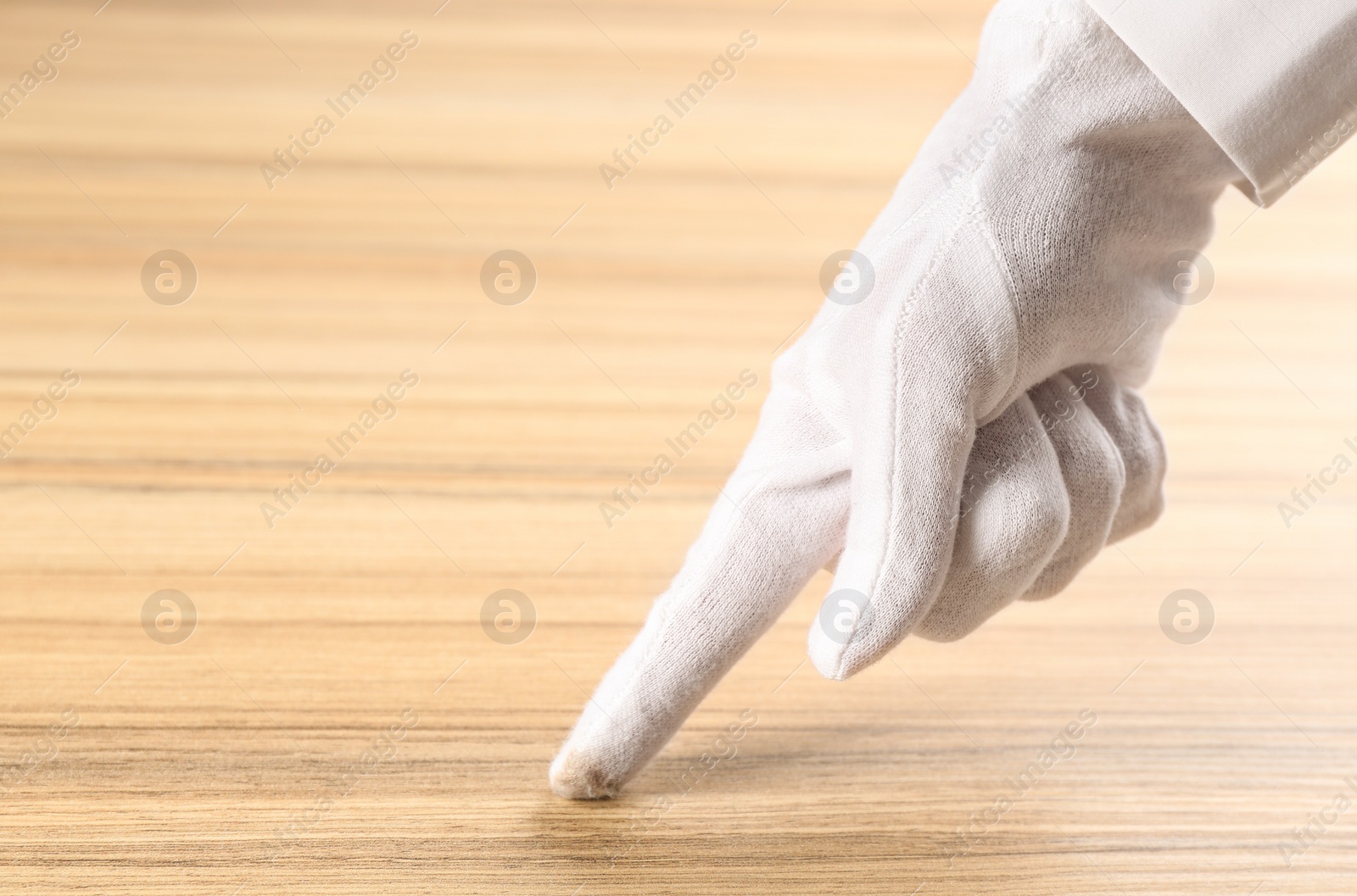 Photo of Person in white glove checking cleanliness of wooden  table, closeup. Space for text