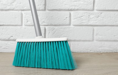 Plastic broom near white brick wall indoors