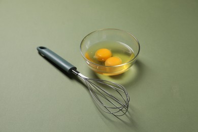 Photo of Metal whisk and raw eggs in bowl on khaki background