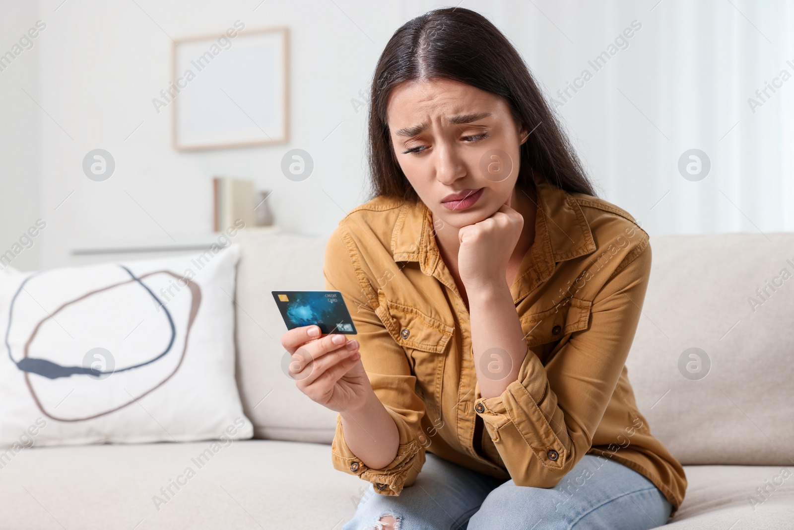 Photo of Confused woman with credit card at home. Be careful - fraud