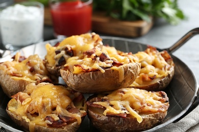 Photo of Frying pan of baked potatoes with cheese and bacon on table, closeup