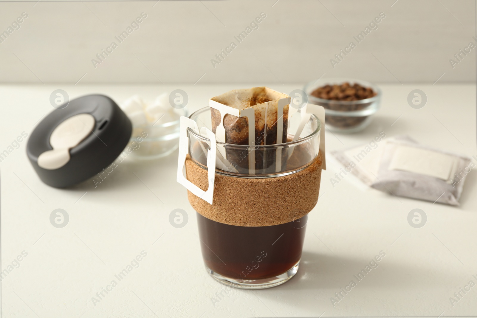 Photo of Glass cup with drip coffee bag on white table