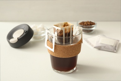 Glass cup with drip coffee bag on white table