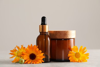 Photo of Bottle and jar of cosmetic products with beautiful calendula flowers on light grey table, closeup