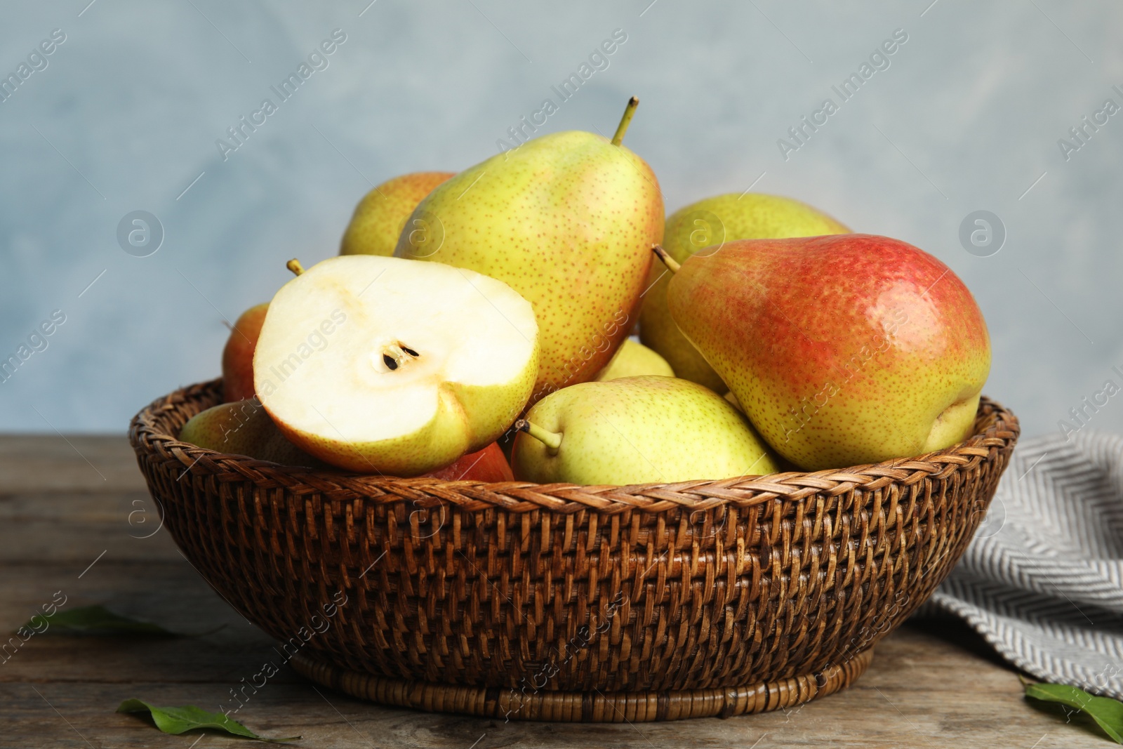 Photo of Wicker basket with ripe juicy pears on brown wooden table against blue background