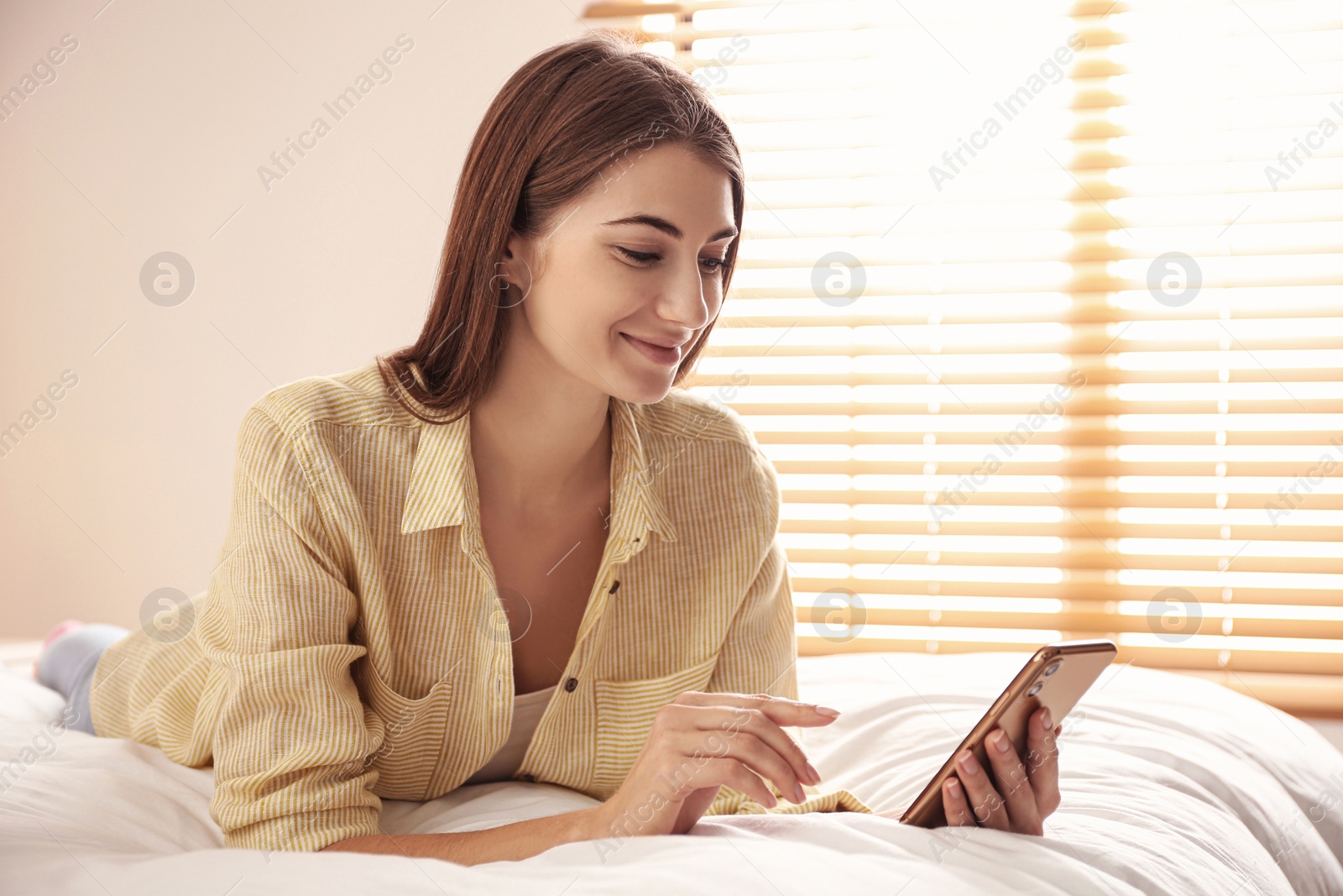 Photo of Young woman using modern smartphone on bed at home