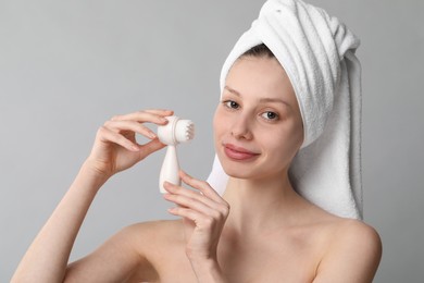 Washing face. Young woman with cleansing brush on grey background