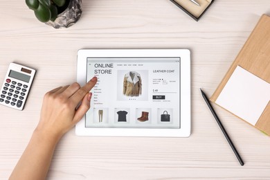 Woman with tablet shopping online at white wooden table, top view