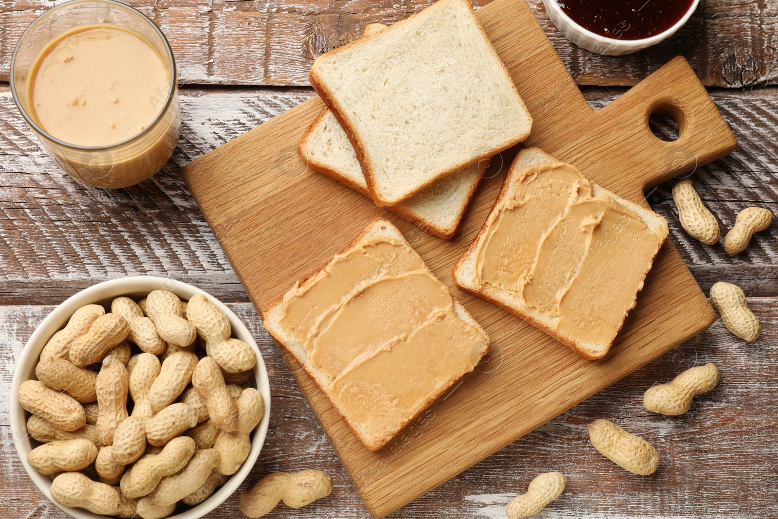 Photo of Tasty peanut butter sandwiches and peanuts on wooden table, flat lay