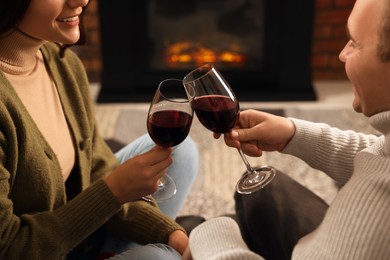 Photo of Happy lovely couple with glasses of wine spending time together near fireplace at home, closeup