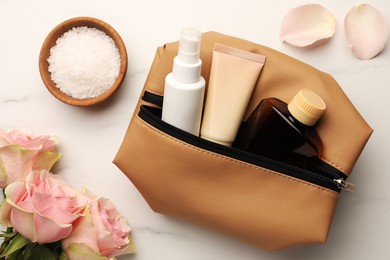 Photo of Preparation for spa. Compact toiletry bag, flowers and different cosmetic products on white marble table, flat lay