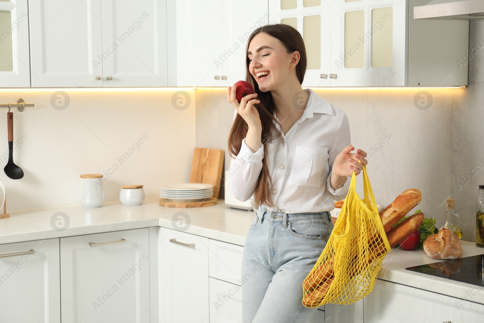 Photo of Woman with string bag of baguettes and apple in kitchen